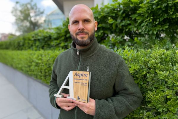 A man stands in front of bushes, holding an award in his hands