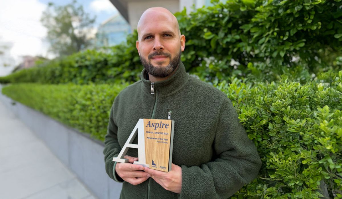 A man stands in front of bushes, holding an award in his hands